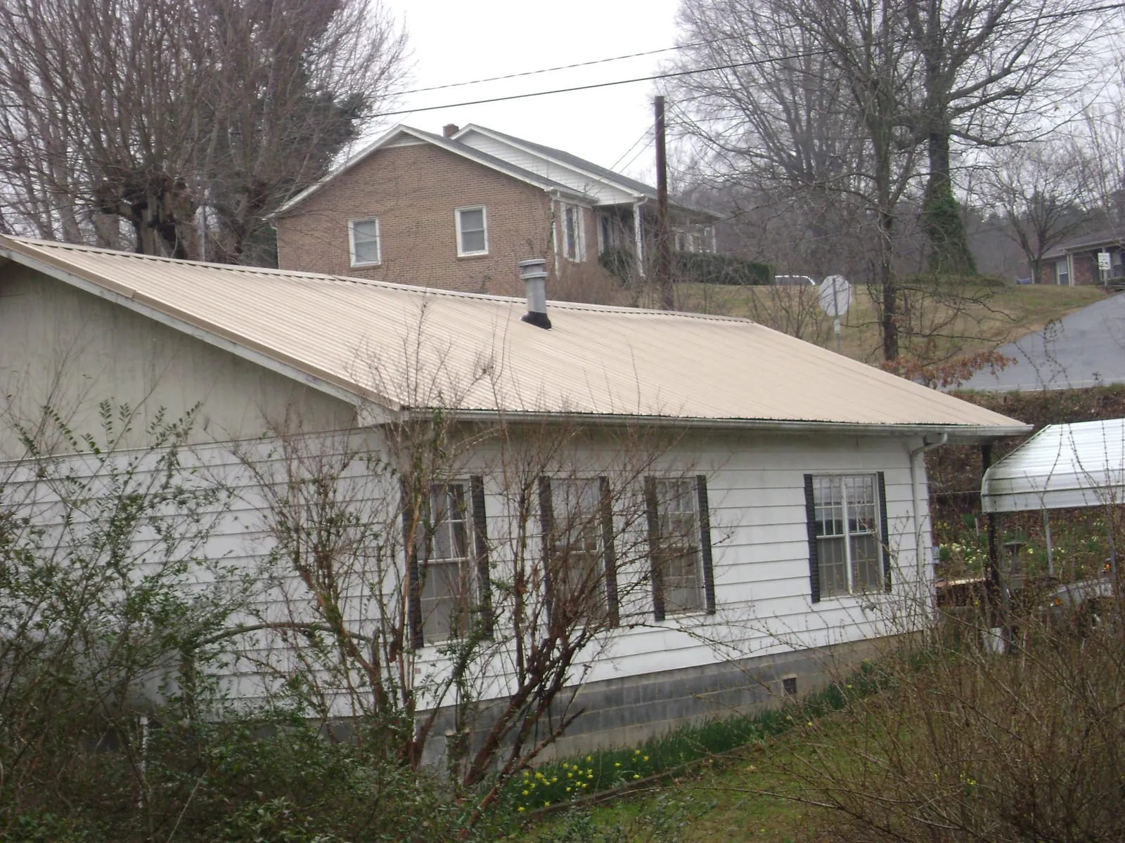 Tan metal roof on a white sided house set into a hillside — Commercial Roofing by Roofing Brothers in Star